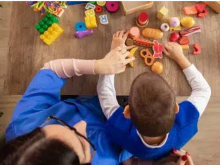 Stručnjakinja i dijete zajedno se igraju edukativnim igračkama za stolom